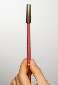 Matita per labbra con un corpo rosa antico opaco e un cappuccio metallico dorato. Il testo recita "SWEED." È visibile una mano che impugna la matita.