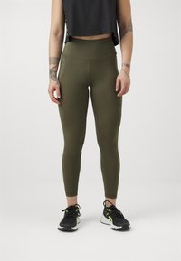 Oliven grønn høy midje leggings laget av elastisk materiale, med en jevn tekstur og et slankt design, paret med svarte treningssko.