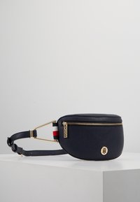 Borsa a tracolla in pelle blu navy con hardware dorato, chiusura con zip e forma rotonda. Presenta una tracolla a righe e un accento del logo sulla parte anteriore.