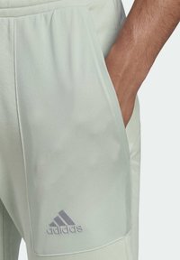 Hellgrüne Sporthose mit weicher Textur, ausgestattet mit einer Seitentasche und einem grauen Adidas-Logo auf der unteren linken Seite.