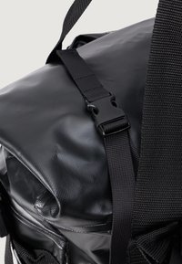 Mochila impermeável preta com uma superfície texturizada, alças ajustáveis e fecho lateral de clip. Design compacto com detalhes minimalistas.