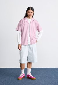 Short-sleeve pink button-up shirt, white long-sleeve shirt underneath, light blue shorts, and pink sneakers with white accents and brown soles.
