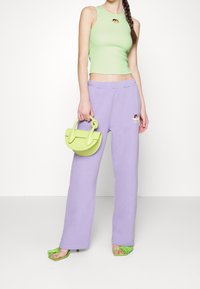 Jasnozielony dopasowany top na ramiączkach z haftowanym detalem, w zestawie z lawendowymi spodniami dresowymi, zieloną torebką i zielonymi sandałami na obcasie z frędzlami.