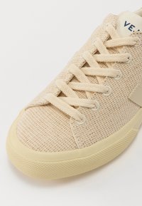 Sneaker in maglia beige con superficie testurizzata, dotata di punta rotonda, lacci piatti e suola in gomma. Marchio visibile sulla linguetta.