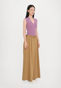 Light purple sleeveless knit top with a V-neck, paired with beige maxi skirt featuring vertical stripes and a belted waist. Pointed cream shoes.
