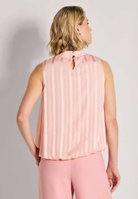 Lichtroze mouwloze top met verticale strepen, voorzien van een keyhole achterkant en een losse pasvorm. Glad oppervlak, zachte stof, minimale hardware.