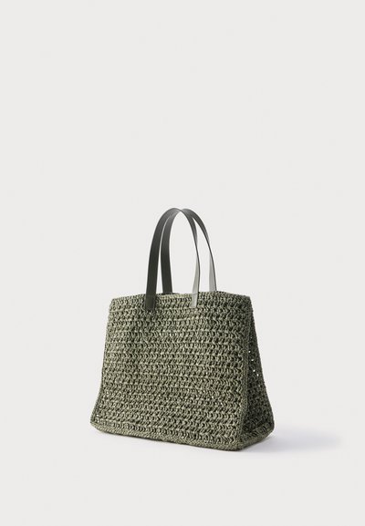 Πράσινη υφαντή τσάντα tote με δύο σκούρες λαβές, ορθογώνιο σχήμα και υφή ανοιχτού πλέγματος σε απλό φόντο.