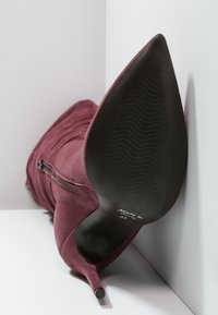 Botín de ante burdeos con tacón de aguja y punta afilada, detalle de cremallera y suela texturizada negra. Talla marcada como 37. Presenta un tacón alto.