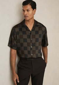 Camisa de botones de manga corta con un patrón de cuadros oscuros, hecha de una tela suave, con un cuello muesca y cuatro botones en la parte frontal.