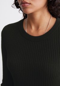 Maglione a coste, di colore verde scuro, con scollo rotondo e tessuto testurizzato, caratterizzato da una collana in argento attorno al collo.