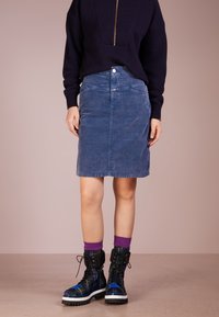 Jeansrock in verblasstem Blau, knielang mit Fronttaschen, kombiniert mit schwarzen und mehrfarbig gemusterten Kampfstiefeln und lila Socken.