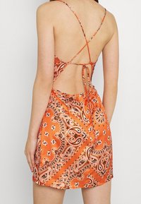 Orangenes Satin-Kleid mit Paisleymuster, verstellbaren Spaghettiträgern, offener Rückansicht und gerafften Details an der Taille.