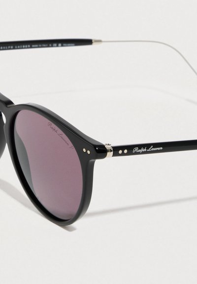 Μαύρα στρογγυλά γυαλιά ηλίου με φακούς με μωβ απόχρωση, χαραγμένο το "Ralph Lauren" στον φακό και στο μπράτσο του σκελετού, σε λευκό φόντο.