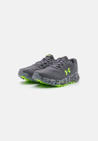 Pantofi de alergare gri cu un superior din plasă texturată, accente de un verde strălucitor și o talpă cu model camuflat care dispune de un design îmbunătățit pentru tracțiune.