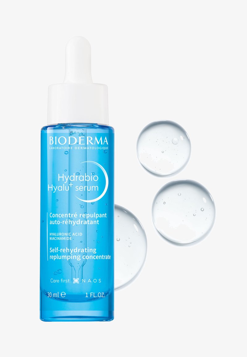 Bioderma Hydrabio Hyalu+ serum in een heldere blauwe glazen fles met een witte pipet. Vergezeld door drie doorschijnende druppels.