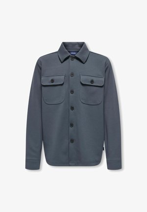 Siva košulja s gumbima od teksturiranog tkanja s dva džepa na prsima i šiljastim ovratnikom. Ima crne gumbe i duge rukave.