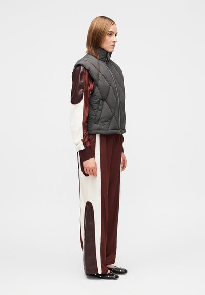 Pihe-puha szürke ujjatlan mellény bordó és krémszínű, fényes részletekkel díszített melegítőnadrág felett, fekete cipőkkel párosítva. Egységesen sima textúrák.