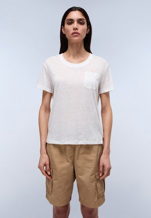 Weißes, kurzärmliges T-Shirt mit strukturiertem Finish und einer Brusttasche. Getragen mit khakifarbenen Cargo-Shorts mit Seitentaschen.