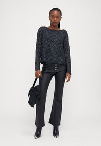 Svart blonde topp med et teksturert blomstermønster, kombinert med høytlivede svarte bukser med tre knapper, og spisse svarte hæler.