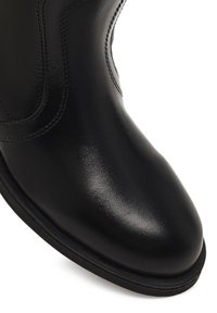 Stivale alla caviglia in pelle nera con una finitura liscia, punta arrotondata e dettagli di cucitura visibili lungo il lato. Suola bassa.