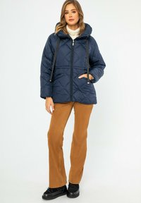 Námornická prošívaná bunda s kapucí, zapínání na zip a černými šňůrkami, spárovaná s hnědými kordovými kalhotami a černými teniskami.