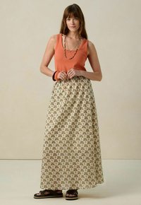 Jupe maxi avec une base crème, ornée d'un motif de palmiers verts et bruns ; associée à un débardeur rouille et des sandales noires. Tissu lisse.