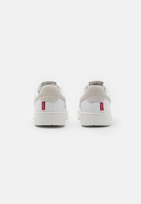 Hvide sneakers med en glat læderoverdel, lysegrå ruskinds detaljer og et rødt logo på hælen. Flad gummisål.