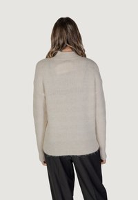 Cremfarbener Strickpullover mit langen Ärmeln, ribbeliziertem Ausschnitt und einem strukturierten, gestreiften Design. Verfügt über eine lockere Passform und einen leicht ausgefransten Saum.