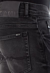 Jeans de mezclilla negra con un parche de cuero con logo en relieve, costuras intrincadas y un diseño de bolsillo distintivo con una etiqueta de la marca.