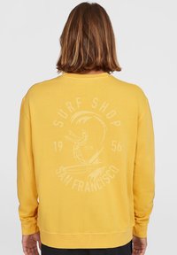 Sudadera de algodón amarilla con cuello redondo acanalado y un estampado gráfico que presenta "SURF SHOP" y un diseño de sirena en la parte posterior.