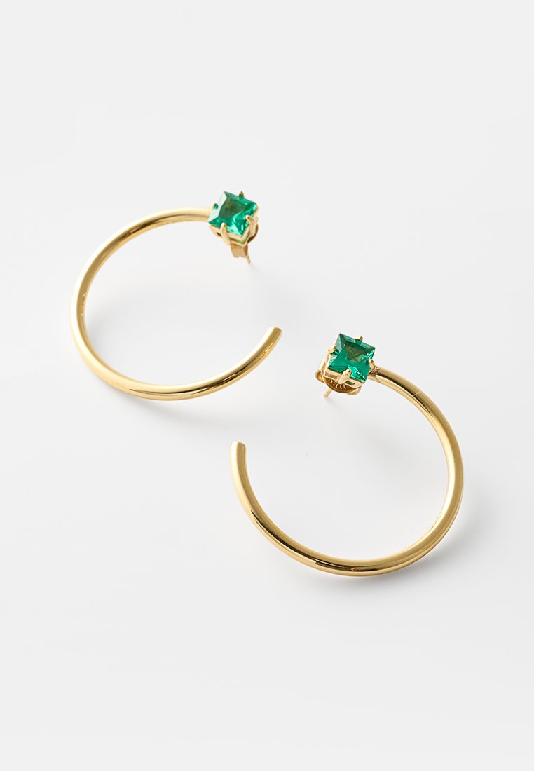 Pendientes de aro abiertos de oro con gemas verdes cuadradas en los postes, exhibidos sobre un fondo blanco.