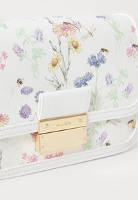 White clutch with floral patterns in pastel colors, featuring a gold-tone clasp and textured leather finish. Subtle bee and dragonfly details.