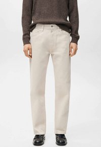 Pantalones de algodón beige claro con corte recto, con bolsillos delanteros y bragueta clásica con botones, combinados con un suéter acanalado marrón oscuro.