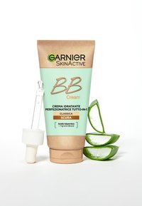 BB cream in un tubo beige e menta, con un tappo a contagocce. Accompagnato da fette fresche di aloe vera, che enfatizzano l'idratazione.
