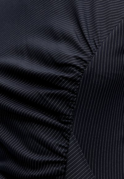 Tissu bleu marine foncé à fines rayures blanches, froncé et plissé sur un côté, montrant à la fois des zones lisses et texturées.