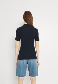 Top in maglia a coste blu navy con maniche corte, silhouette aderente, abbinato a pantaloni shorts in denim azzurro. Design semplice, bordi senza cuciture.