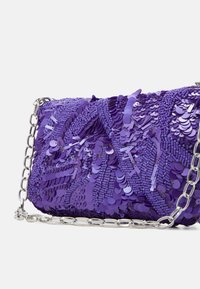 Fioletowa kopertówka ozdobiona cekinami z misternym koralikowym wykończeniem i srebrnym łańcuszkiem na białym tle.