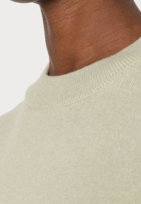 Jasnozielony sweter dziany z okrągłym dekoltem, charakteryzujący się miękką teksturą i równymi szwami wzdłuż kołnierza i ciała.