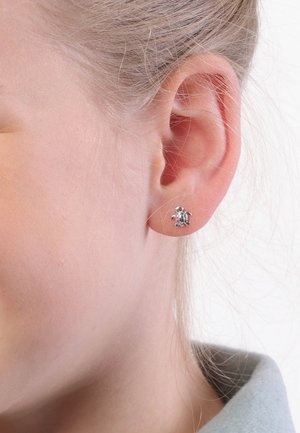 Silberne, schildkrötenförmige Ohrstecker, die am Ohrläppchen präsentiert werden, mit detaillierten Gravuren und einer polierten Oberfläche.