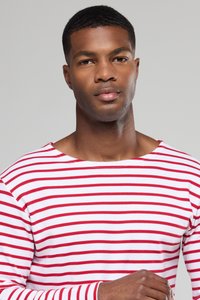 Langærmet skjorte i hvid med røde vandrette striber. Har en bred halsudskæring og et blødt, struktureret bomuldsstof.