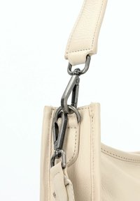 Beige leren handtas met een gestructureerde afwerking. Voorzien van zilveren metalen hardware en een stevige strap met een haaksluiting voor bevestiging.