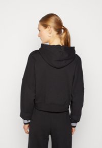 Black cropped hoodie with a drawstring hood, featuring ribbed cuffs with white stripes. Smooth texture, relaxed fit, and minimalistic design.