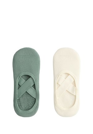 Paire de chaussons invisibles avec des brides élastiques croisées, un vert et un blanc cassé, vus de dessus sur fond blanc.