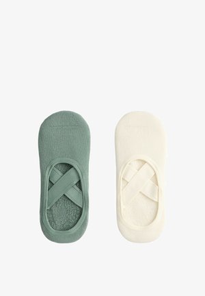 Paire de chaussons invisibles avec des brides élastiques croisées, un vert et un blanc cassé, vus de dessus sur fond blanc.