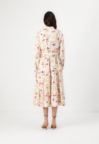 Rochie lungă cu imprimeu floral dintr-un material moale, având mâneci lungi, talie ajustată și fustă în straturi. Fundal deschis cu culori vibrante.