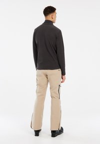Lichtgewicht, donkergrijze fleece pullover met een hoge kraag, gecombineerd met beige broeken met zijrits zakken en zwarte accenten.