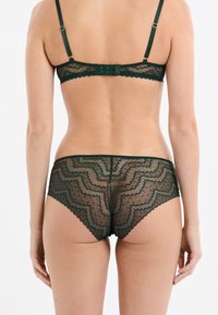 Set in pizzo verde con bordi scallop, un motivo a zigzag, spalline regolabili e chiusura a gancio sul reggiseno, abbinato a perizoma in pizzo.