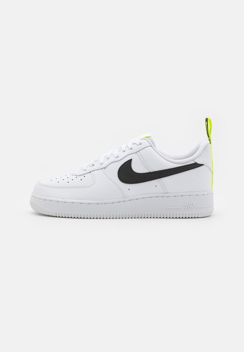 White Nike Air Force 1 sneakers feature a black swoosh, textured leather upper, and a neon yellow accent on the heel tab. Classic low-top design.