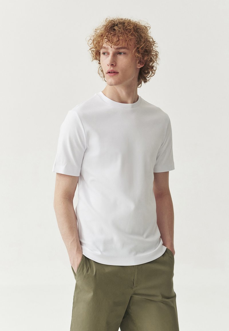 Hvid kortærmet t-shirt med rund hals, lavet af glat stof. Båret med olivengrønne bukser med en afslappet pasform.