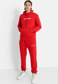 Röd hoodie och sweatpants-set, med en framficka, snörning i huvan och vit logotext. Tillverkad av mjukt tyg med en avslappnad passform.